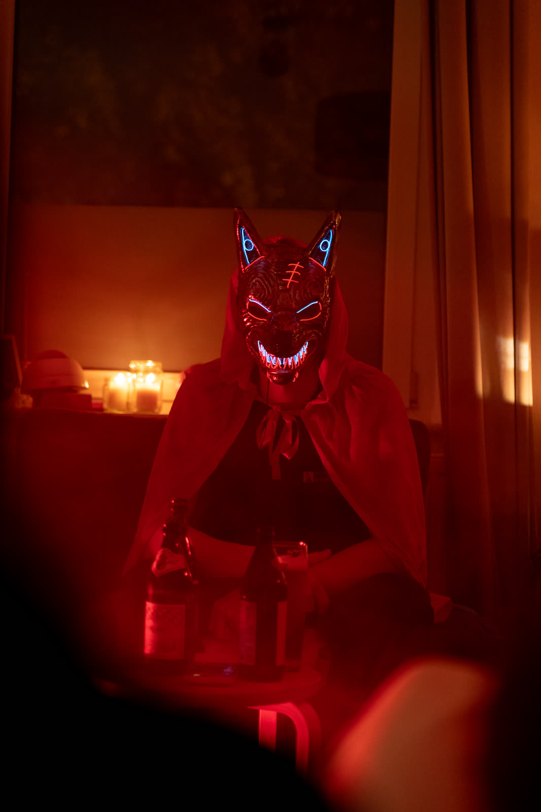 Person mit leuchtender Werwolf-Maske und rotem Umhang am Tisch, dahinter Kerzen