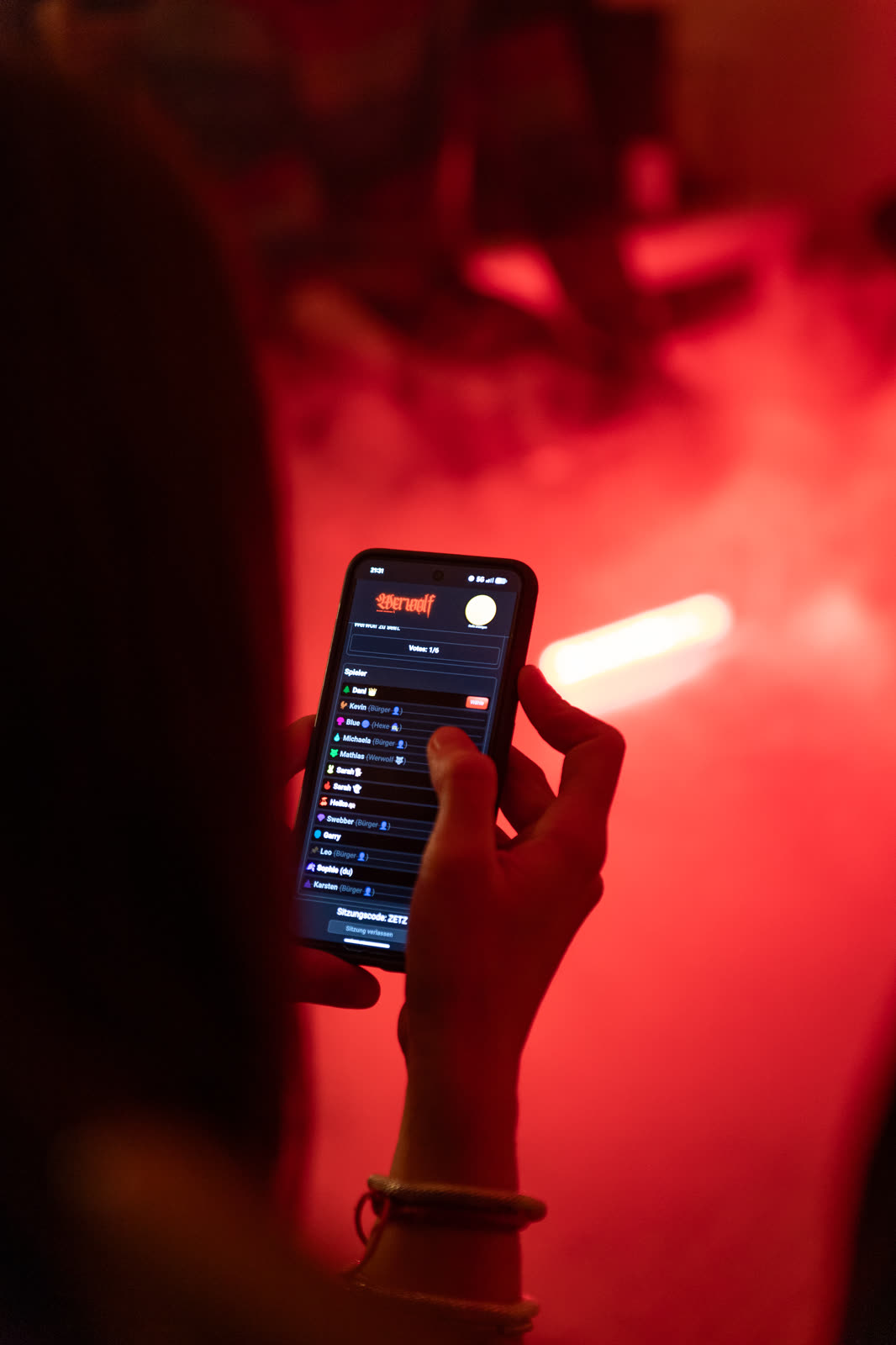 Spielerin hält ihr Handy mit der Spielerliste von play.7wolf.de, im Hintergrund roter Nebel